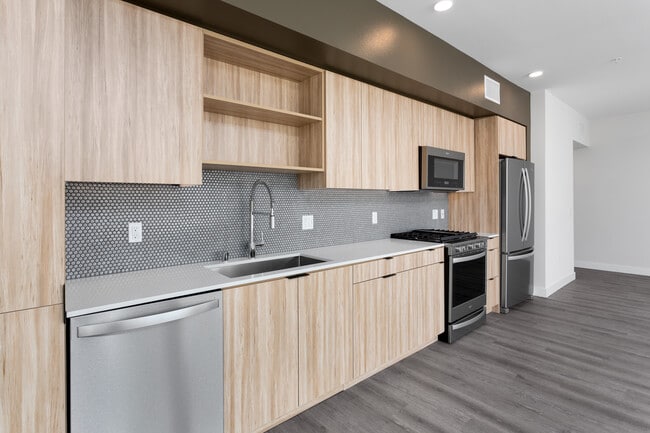 Open concert kitchen with quartz countertops backsplash, stainless steel appliances and hard surface flooring - AVA Hollywood at La Pietra Place