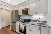 Renovated Package II kitchen with stainless steel appliances, light grey quartz countertops, white shaker cabinetry, and hard surface flooring - eaves Thousand Oaks Apartments