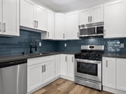 Blue tiled kitchen with stainless steel fridge, oven, and microwave. - Palms Court Apartments