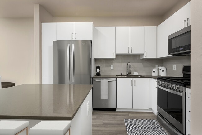 Renovated Package I kitchen with quartz countertops, white cabinetry, stainless steel appliances, hard surface vinyl plank flooring, and tile backsplash - Avalon Playa Vista