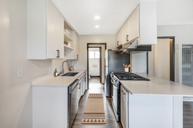 Renovated Package I kitchen with stainless steel appliances, white quartz countertops, white cabinetry, and hard surface flooring (select homes) - AVA Burbank
