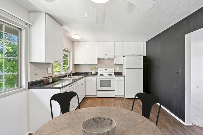Kitchen with white cabinetry, black laminate countertops, white appliances, and hard surface flooring - AVA Newport Apartments
