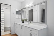 Renovated Package II bath with white quartz countertops, white cabinetry, updated hard surface flooring, and framed mirror - AVA Pacific Beach
