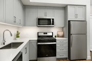 Apartments with modern kitchens featuring grey cabinetry, white quartz stone countertops, white tile backsplash, stainless steel appliances, and hard surface flooring - Avalon Monrovia Apartments