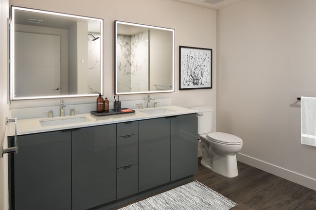 Upgrade Package Bath with grey cabinetry, white quartz countertop, marble shower surround, and lit vanity mirror - AVA Arts District