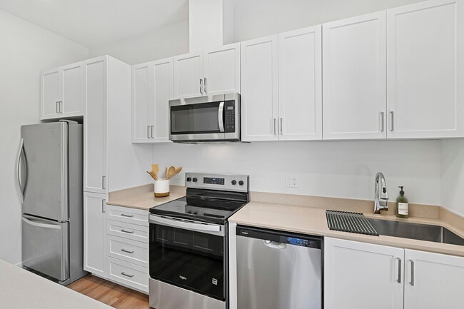 Freestanding Home kitchen with stainless steel appliances, white cabinetry, beige quartz countertops, and hard-surface flooring - eaves San Marcos