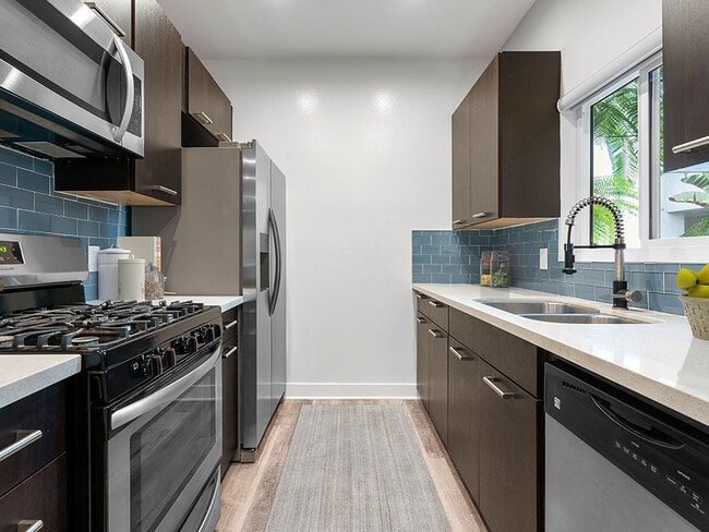 Blue tiled kitchen with granite countertop and stainless steel fridge, microwave, and fixtures. - South Hayworth Lofts