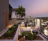 Chic rooftop terrace with cozy seating, lush planters, and stunning city skyline views at dusk. - Ancora