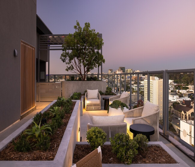 Chic rooftop terrace with cozy seating, lush planters, and stunning city skyline views at dusk. - Ancora