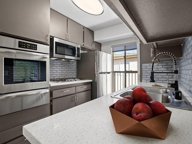 Blue tiled kitchen with stainless steel oven, microwave, fridge, and fixtures. - Tilden II Apartments