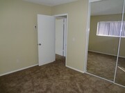 Carpeted bedroom with large window and mirrored door closets at Villa Knolls Apartments in La Mesa, California. - Villa Knolls Apartments