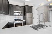 Kitchens with dark cabinetry, white quartz countertops, white tile backsplash, stainless steel appliances, and hard surface flooring - AVA Balboa Park Apartments