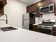 White tiled kitchen with modern faucet, stainless steel appliances, and refrigerator. - Bonita Terrace Apartments