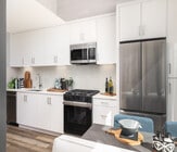 Bright, modern kitchen with sleek stainless steel appliances, abundant white cabinetry, and stylish wood flooring. Perfect for culinary creativity. - Ancora