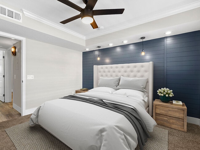 Carpeted bedroom with ceiling fan and textured shiplap accent wall. - Catalina Apartments