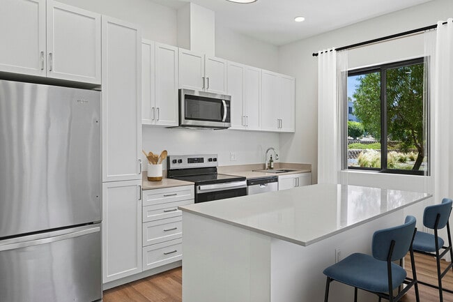 Freestanding Home kitchen with stainless steel appliances, white cabinetry, beige quartz countertops, and hard-surface flooring - eaves San Marcos Rental