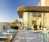 Luxurious rooftop pool area with sleek lounge chairs, panoramic city views, and modern glass-encased lounge in a vibrant high-rise setting. - Ancora